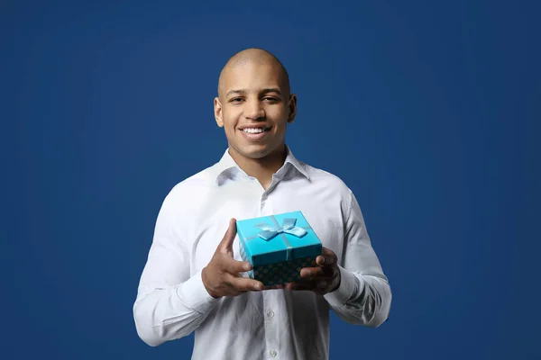 Handsome African-American man with gift on color background — Stock Photo, Image