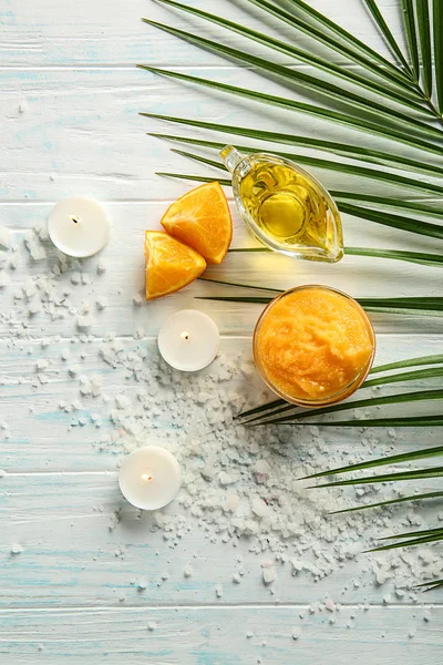 Bowl with orange body scrub, candles and essential oil on white wooden background