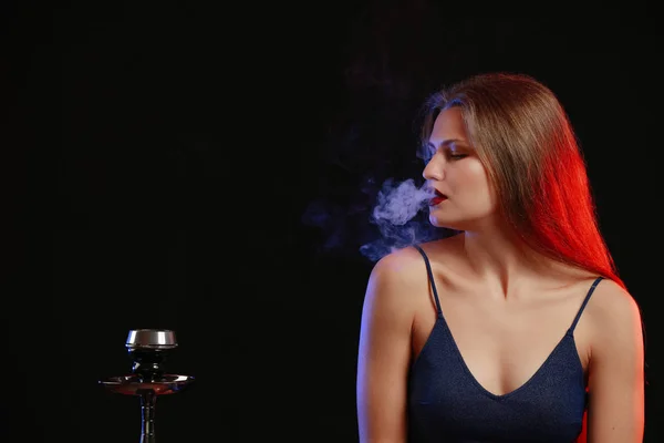 Jovem mulher fumando narguilé no fundo escuro — Fotografia de Stock
