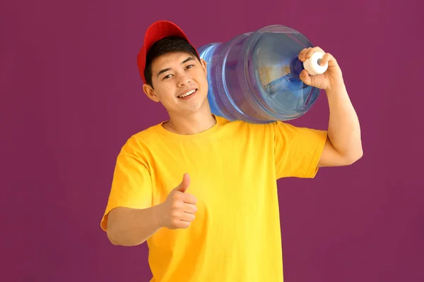 Azjatycki dostawa kurierem z butelką wody pokazując kciuk-up gest na kolorowym tle — Zdjęcie stockowe