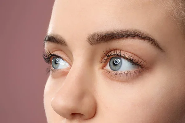 Vacker ung kvinna med laminerade ögonfransar på färg bakgrund, närbild — Stockfoto
