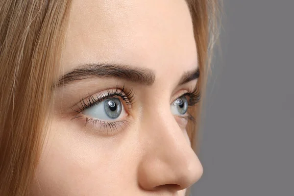 Beautiful young woman with laminated eyelashes on grey background, closeup