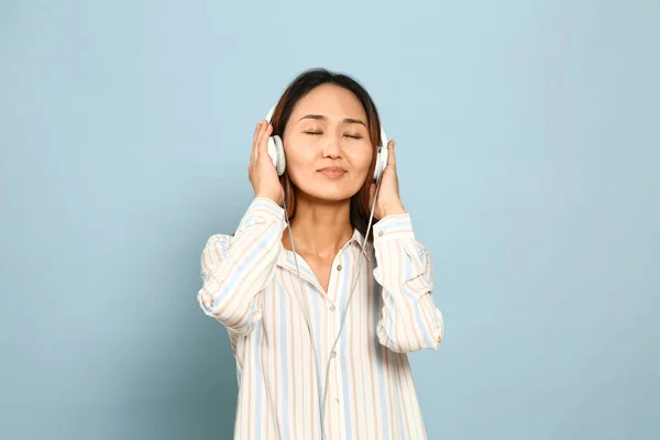 Asian woman listening to music on color background — Stock Photo, Image