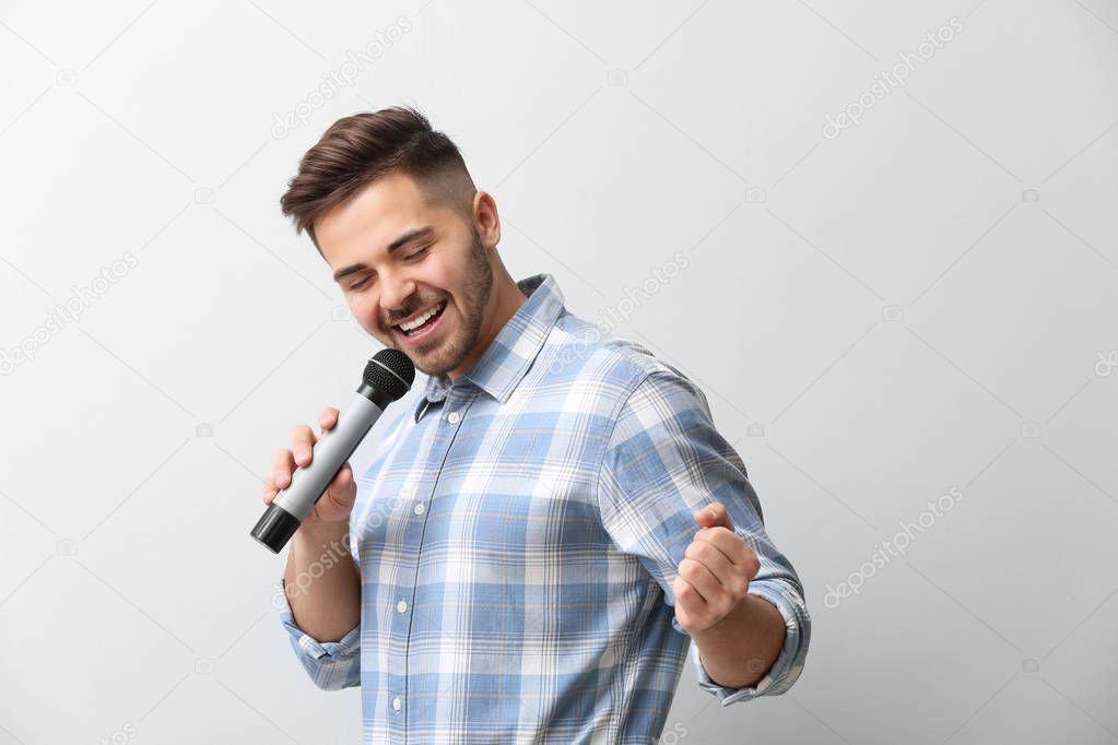 Handsome male singer with microphone on light background