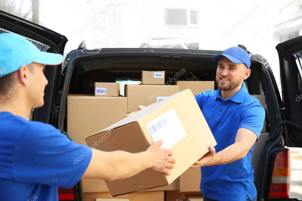 Delivery men taking parcels from car outdoors