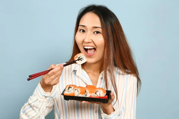 Asian woman eating sushi on color background — Stock Photo, Image