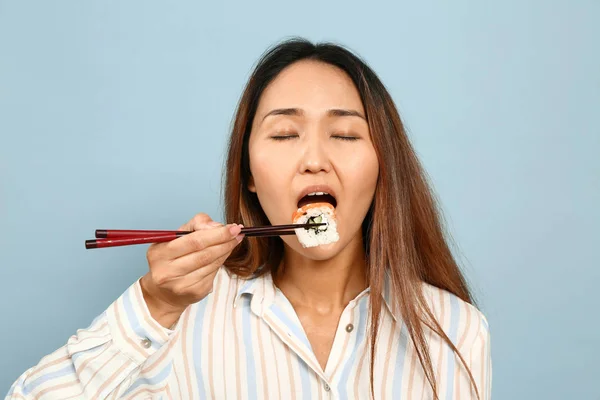 Aziatische vrouw eten sushi op kleur achtergrond — Stockfoto