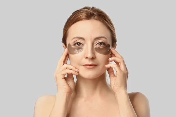 Volwassen vrouw met onder-oog patches op lichte achtergrond — Stockfoto
