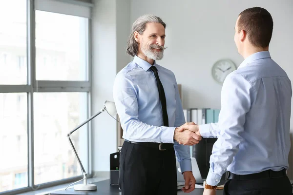 Mature businessman shaking hands with young colleague in office — Stock Photo, Image