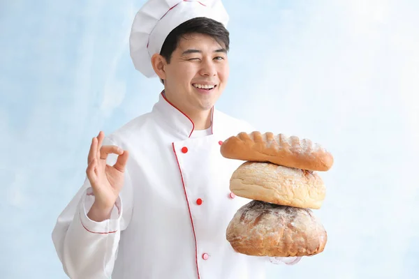 Padeiro asiático com pão fresco mostrando gesto OK no fundo de cor — Fotografia de Stock