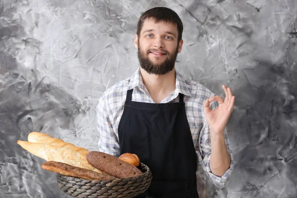 Młody piekarz ze świeżym chlebem pokazuje Ok gest na tle koloru — Zdjęcie stockowe