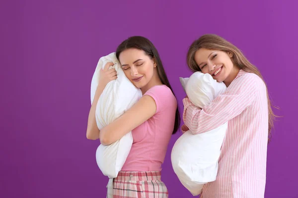 Mooie jonge vrouwen in pyjama en met kussens op kleur achtergrond — Stockfoto