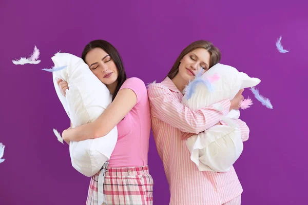 Piękne młode kobiety w piżamie i poduszki na tle koloru — Zdjęcie stockowe