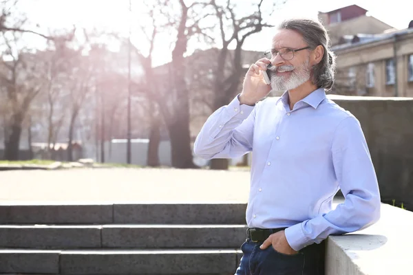 Handsome mature businessman talking by mobile phone outdoors — Stock Photo, Image