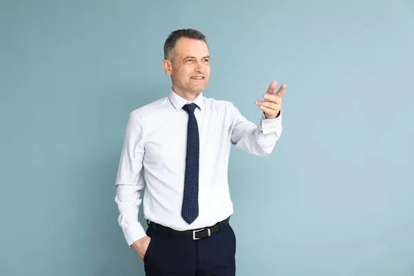 Handsome mature businessman pointing at something on color background — Stock Photo, Image