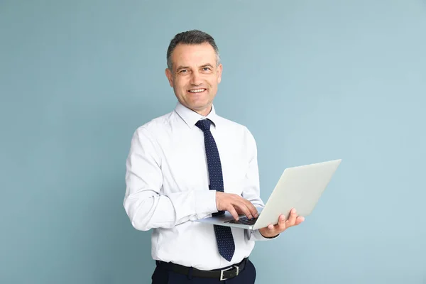 Красивый зрелый бизнесмен с ноутбуком на цветном фоне — стоковое фото
