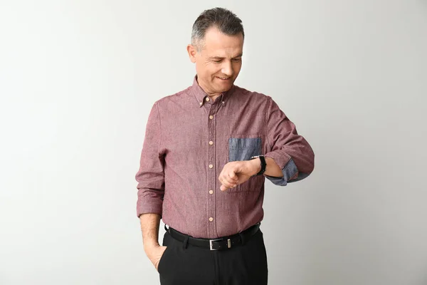 Handsome mature businessman looking at watch on light background — Stock Photo, Image