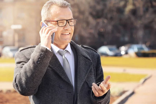 Knappe volwassen zakenman praten via de telefoon buitenshuis — Stockfoto