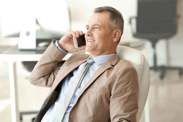 Handsome mature businessman talking by phone in office — Stock Photo, Image