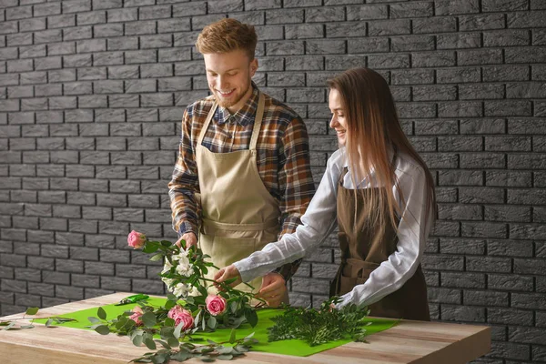 Floristas fazendo buquê à mesa contra fundo escuro — Fotografia de Stock