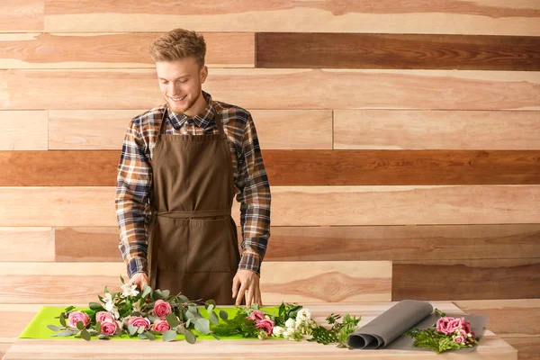 Male florist making bouquet at table against wooden background — Stock Photo, Image