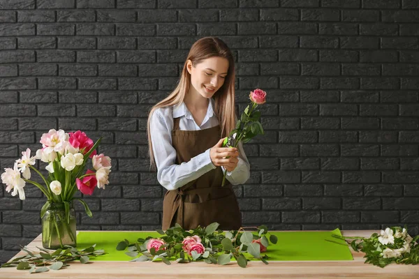 Florista fazendo buquê à mesa contra fundo escuro — Fotografia de Stock