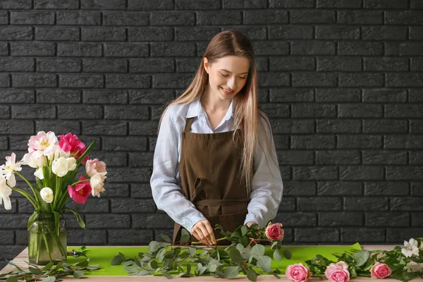 Florist making bouquet at table against dark background — Stock Photo, Image