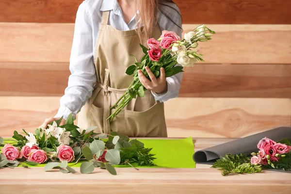 Florista fazendo buquê à mesa contra fundo de madeira — Fotografia de Stock