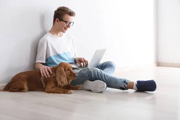 Adolescente chico con lindo perro y portátil sentado cerca de la pared de luz —  Fotos de Stock