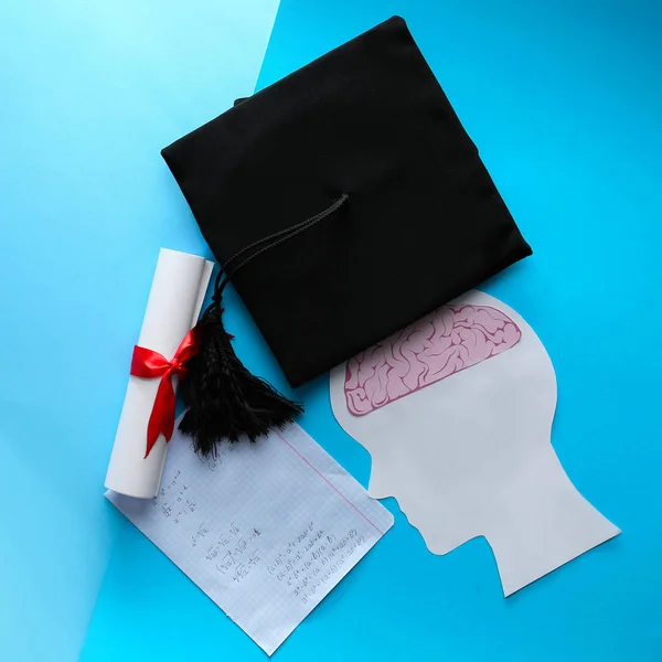 Mortar board with diploma, human head with brain and sheet of paper on color background. Concept of high school graduation — Stock Photo, Image