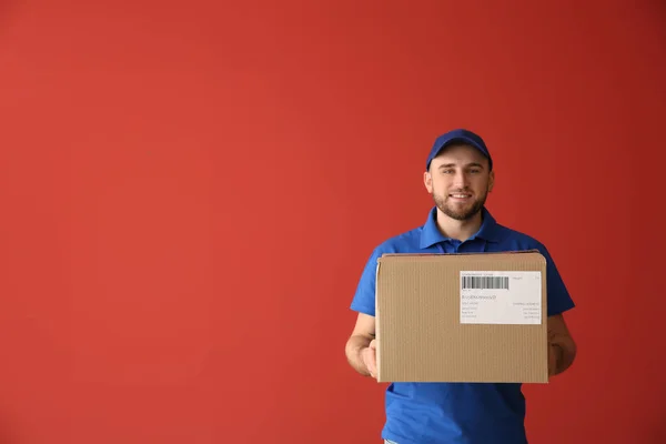 Handsome delivery man with box on color background