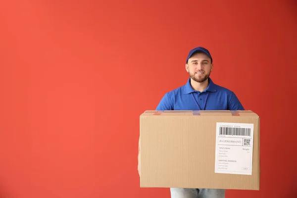 Bonito homem de entrega com parcela em fundo de cor — Fotografia de Stock