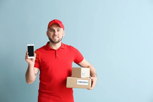 Handsome delivery man with boxes and mobile phone on color background