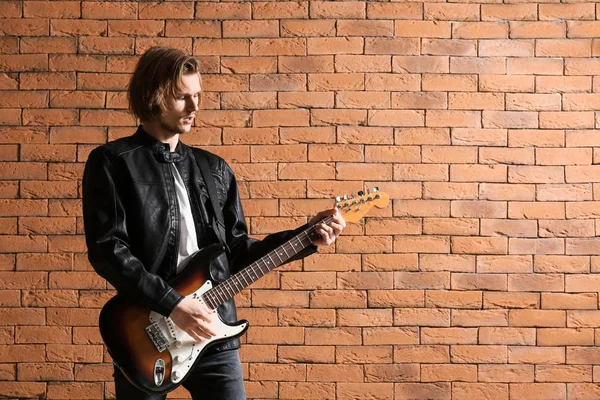 Bello giovane che suona la chitarra contro il muro di mattoni — Foto Stock