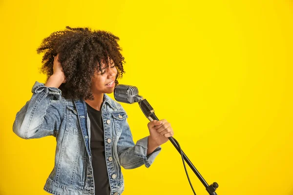 Fille afro-américaine avec microphone chantant sur fond de couleur — Photo