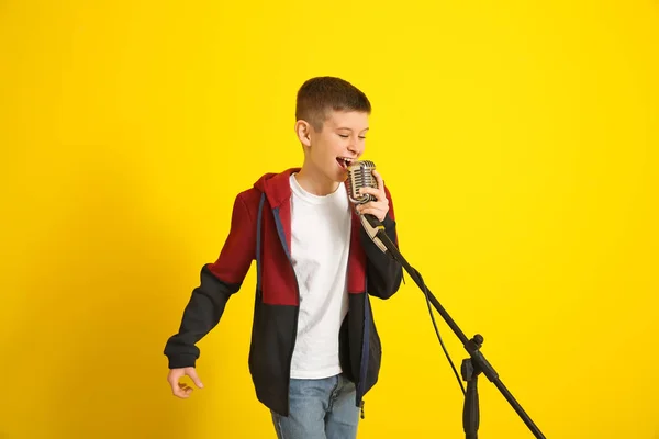 Mladý chlapec s mikrofonem zpívající na barevném pozadí — Stock fotografie