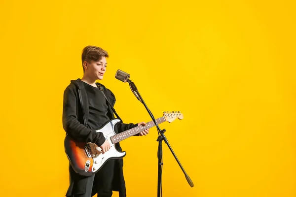 Teenage boy with microphone singing and playing guitar against color background — Stock Photo, Image