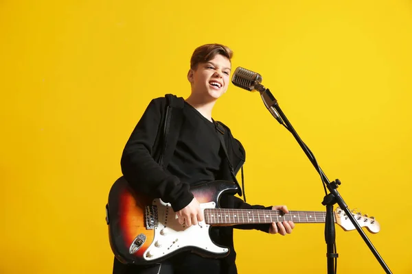 Teenage boy with microphone singing and playing guitar against color background — Stock Photo, Image