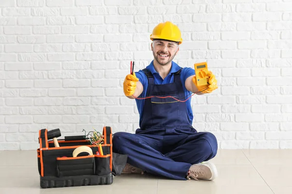 Electricista masculino con kit de herramientas sentado cerca de la pared de ladrillo blanco — Foto de Stock