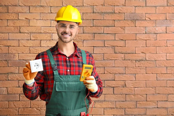 Electricista masculino con multímetro y zócalo cerca de la pared de ladrillo —  Fotos de Stock