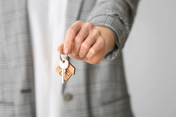 Agente inmobiliario femenino con llave sobre fondo gris, primer plano — Foto de Stock