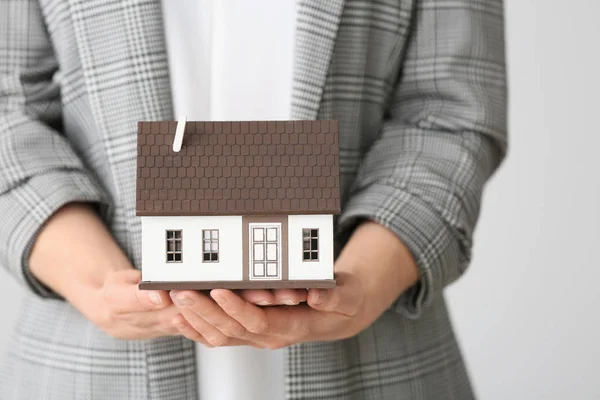 Female real estate agent with house model on grey background, closeup — Stock Photo, Image