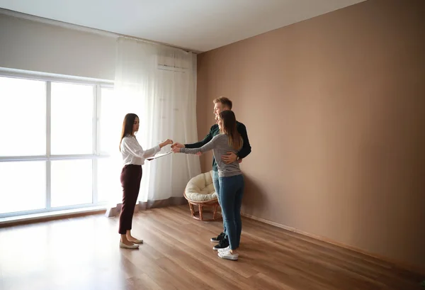 Inmobiliaria dando una llave de casa nueva a pareja joven — Foto de Stock