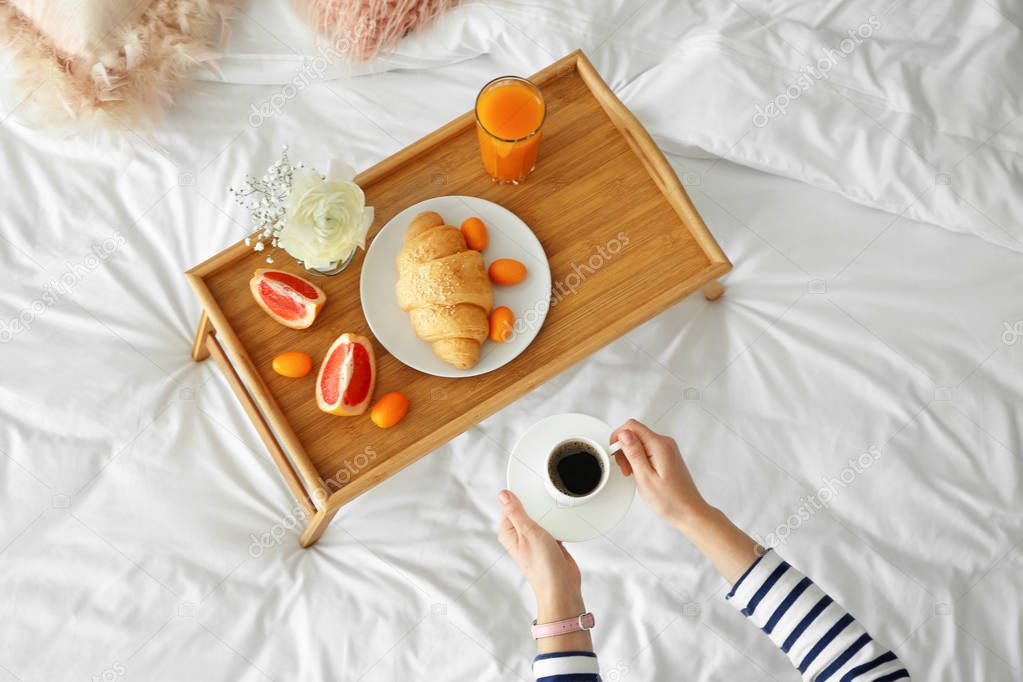 Woman having breakfast with croissant and coffee on bed at home