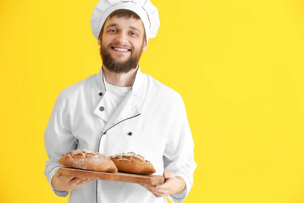 Young baker with fresh bread on color background — 스톡 사진