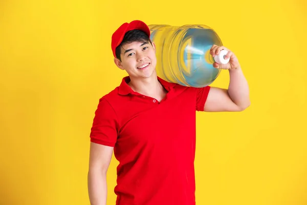 Asian delivery courier with bottle of water on color background — Stock Photo, Image