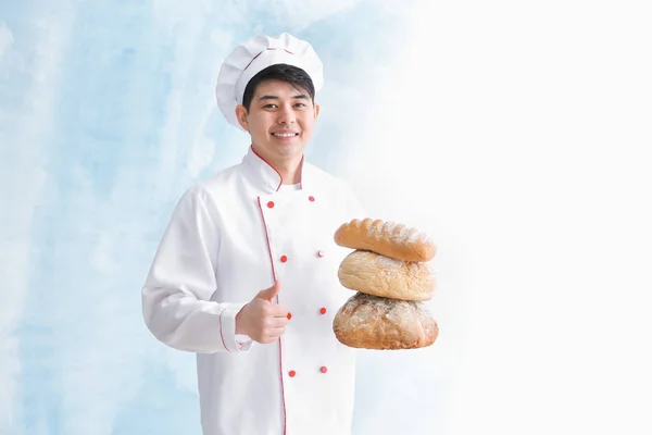 Padeiro asiático com pão fresco mostrando gesto de polegar para cima no fundo de cor — Fotografia de Stock