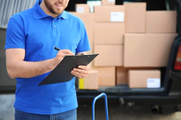 Handsome delivery man with clipboard outdoors