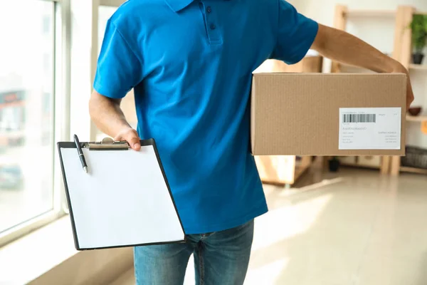 Delivery man with box and clipboard indoors
