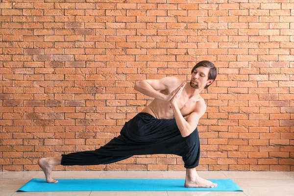 Sporty man practicing yoga against brick wall — Stock Photo, Image